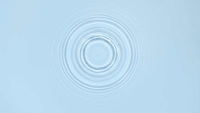 White drop falls down creating circles on water surface on pale blue background | Background shot for skin care cosmetics commercial Royalty-Free Stock Footage #1077025592