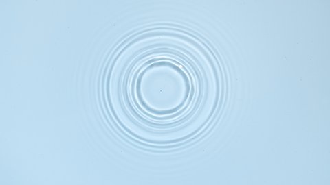 White drop falls down creating circles on water surface on pale blue background | Background shot for skin care cosmetics commercial