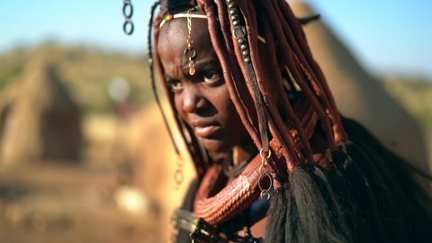 Himba woman in traditional village in Namibia, Africa, slow motion shot. The Himba are famous for their use of otjize, a paste of butter, fat and red ochre, which they apply to their hair and skin.