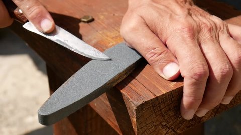 Close-up of beautiful man's hands sharpening a knife with a whetstone