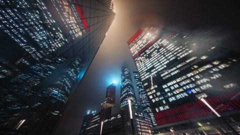 Beautiful motion timelapse of Moscow City towers at night. View from the bottom to overhanging skyscrapers of Business Center with illuminated windows and neon lights glittering in rare raindrops.