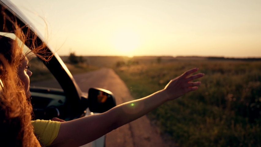 Happy girl in car window. Hair in wind. Girl travels by car. Hand in sun. Windy breeze from car window. Happy girl smiling from car window. Windy breeze in your hair. Hand in the rays of the sun | Shutterstock HD Video #1077035294