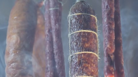 In detail. Salami and cervelat sausages are smoked in intense smoke. Close-up, brown wooden background. View from below. Smoking and drying meat products.