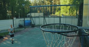 Male basketball player on court running with ball and successfully throwing ball to the net outdoors, slow motion