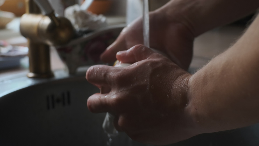 Close up view man washes white glass in old kitchen. Thorough cleaning of dishes under running water using soap and detergents. white mug or cup becomes clean after washing. Royalty-Free Stock Footage #1077040235