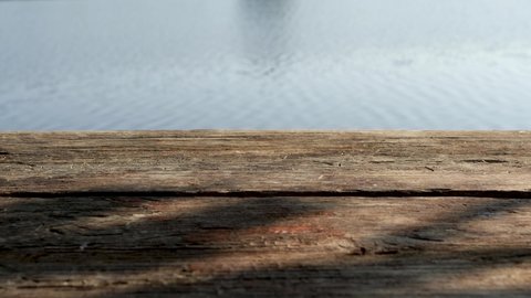 Closeup view 4k stock video footage of old vintage organic wooden weathered planks with tree shadows isolated on sunny blurry defocused blue river water backdrop. Abstract background with copy space