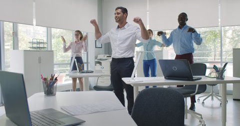 Group of happy young diverse businesspeople doing stretching exercise in office. Multiethnic colleagues doing fitness exercise at workplace in modern open space workplace