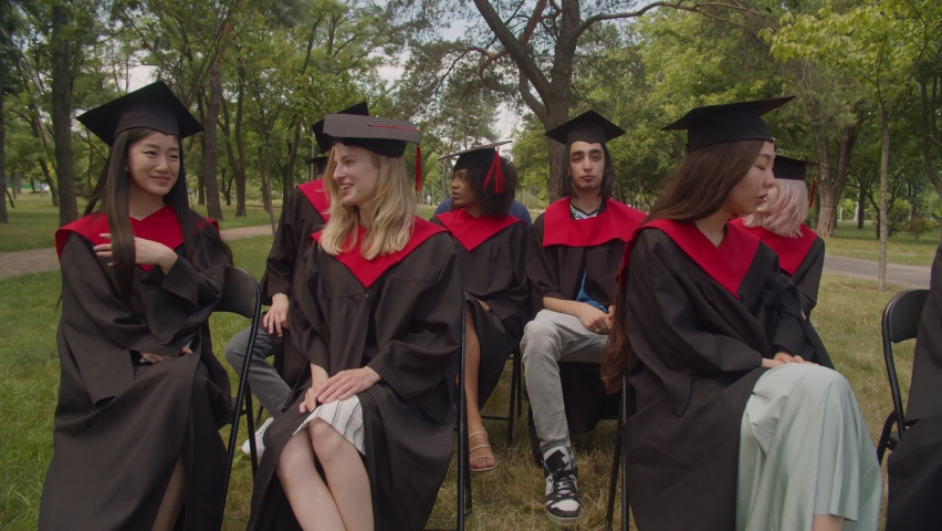 Group of excited diverse multiracial graduates in academic gowns and mortarboards posing for selfie shot on cellphone, expressing carefree mood and happiness during outdoor graduation ceremony. | Shutterstock HD Video #1077055562