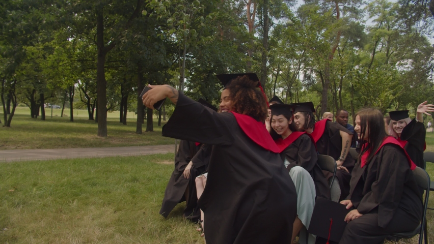 Group of joyful attractive diverse multiethnic students in graduation gowns and mortarboards recording video content on smart phone, expressing happiness and excitement at graduation day. | Shutterstock HD Video #1077055574