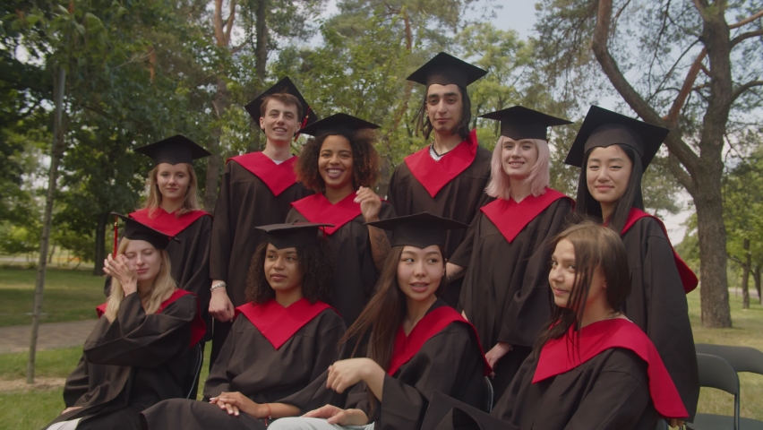 Group of positive attractive diverse multiethnic graduates in graduation gowns and mortarboards posing for picture together, expressing happiness and cheerful mood after graduation ceremony. | Shutterstock HD Video #1077055583