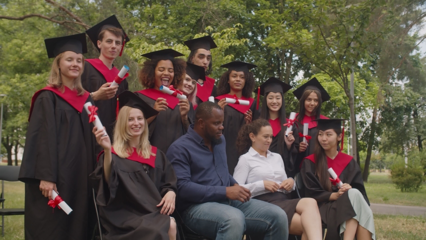 Group of excited diverse multiracial graduates in graduation gowns and mortarboards showing diplomas with pride, expressing happiness and joy while celebrating graduation day with academic staff. | Shutterstock HD Video #1077055598
