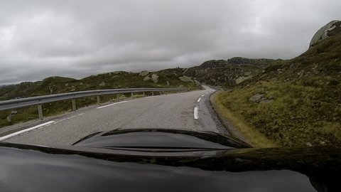 A black car driving in the Norwegian mountains in the summertime. Slow motion POV shot. Action camera mounted on the top of the car.