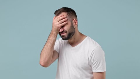 Sad upset ashamed tired young brunet man 20s wears white t-shirt put hand on face facepalm epic fail mistaken omg gesture isolated on pastel light blue background. People emotions lifestyle concept
