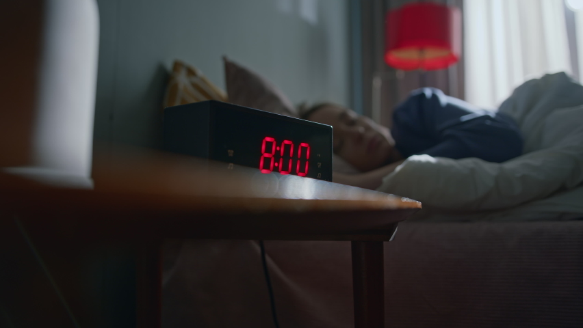 Pretty girl sleeping in bed at home wakes up to digital alarm clock on bedside table and tries to disable it without opening her eyes. She covers up in blanket to sleep in. Slow motion cinematic shot Royalty-Free Stock Footage #1077057674