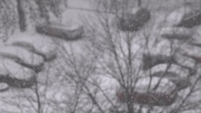 Snowy winter weather in city. Closeup view stock video footage of white fluffy snowflakes flying in air isolated on blurry city street view