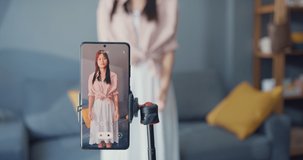 Happy young Asian girl blogger front of phone camera record video enjoy with dance content in living room at home. Social distance coronavirus pandemic concept. Freedom and active lifestyle concept