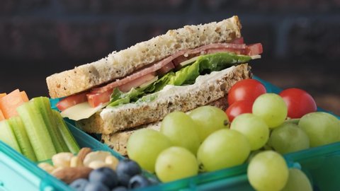 Healthy school or work lunch box with sandwich, fresh vegetables, fruits and nuts. Rotating video