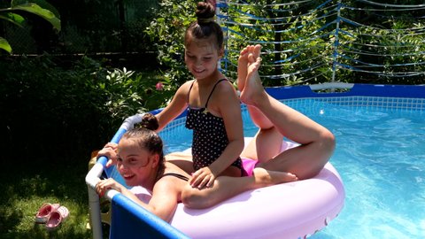 Happy children splash down from swim ring in outdoor swimming pool, fun