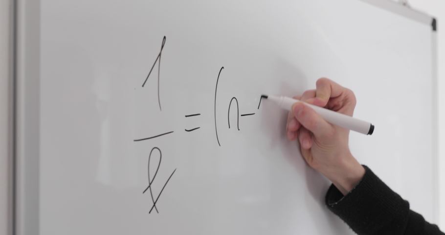 Student writing formulas on whiteboard. Hand with black marker wrote physics formulas on whiteboard closeup