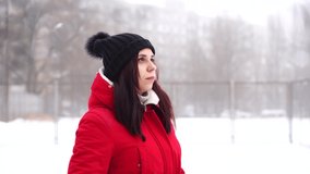 young woman in hat and red jacket, standing on street. Adult brunette warms in cool weather on walk in winter season