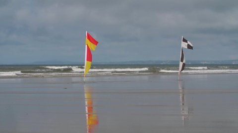 4K CU Shot of two beach safety flags black, white, yellow, and red colours indicating where is safe for swimming or board sports like surfing directing tourists away from dangerous rip currents 