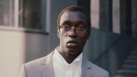 Black handsome young entrepreneur in corporate suit posing to camera near contemporary office building. Modern business people. African ethnicity.