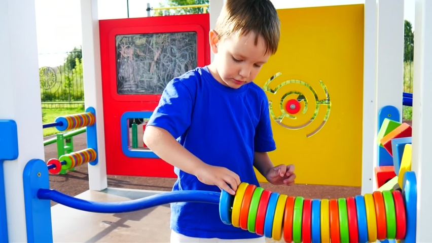 A cute boy moves big colorful abacus rings on the playground outdoors