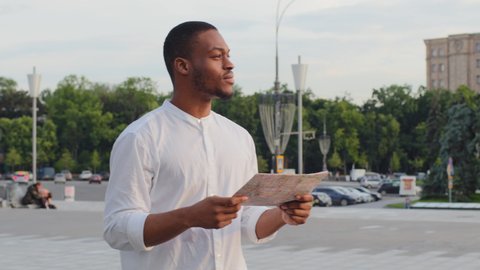Male tourist foreign international student lost afro american man african guy traveler in new city standing on street outdoors with map searching way road destination navigation route looking around