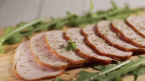 Traditional ham on a wooden cutting board. Thin slices of meat are sprinkling with herbs. Concept of delicious food snacks and cooking.