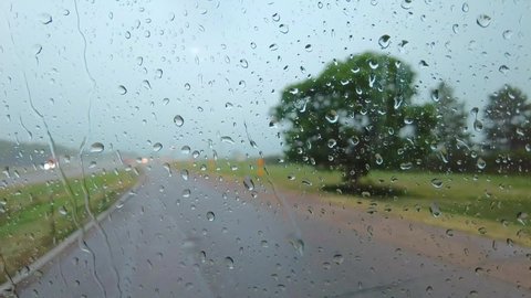 Time Lapse of rain and hail hitting a large windshield while vehicle is waiting out the rain storm at a rest area along the interstate; driver seeking shelter from the storm