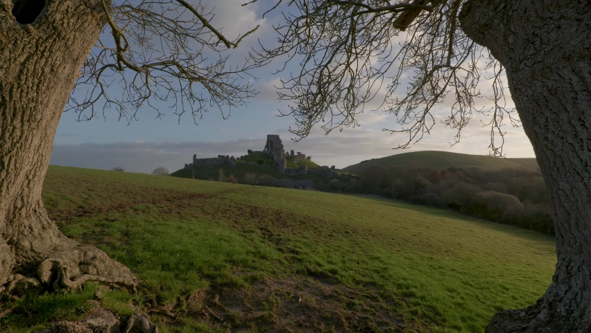 Slow zoom in shot of Corfe Castle framed by trees in the early morning light.