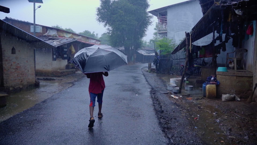Slowmotion of a Indian village boy walking in the rain with an umbrella on a lonely street during pandemic