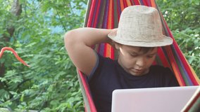 boy in a hammock uses a laptop. Communicates online on vacation. resting in a hammock, drinking a cocktail. Works online. Leads the stream. Plays a video game. Blogger