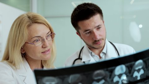 Close-up male doctor and female colleague examining patient chest x-ray film lungs scan at radiology department in hospital. Covid-19 xray test, covid worldwide virus epidemic slow motion concept.