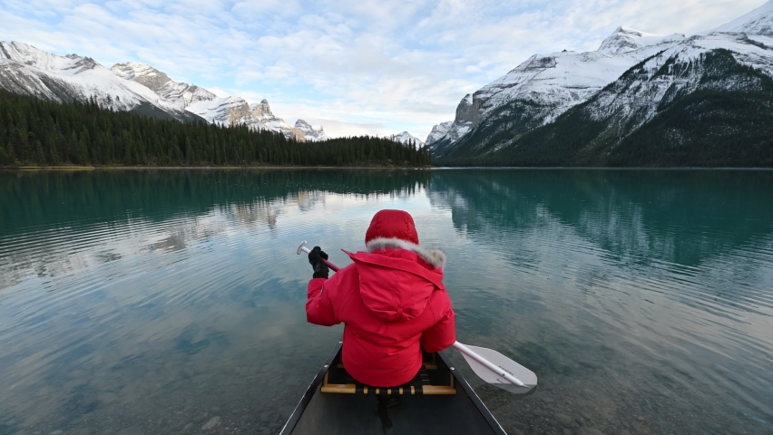 Tourist in winter coat holding oar in a canoe on Maligne lake near Spirit island at Jasper national park. Leisure activity, Recreational pursuit