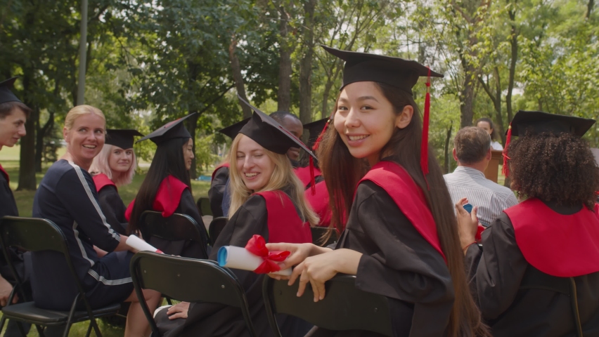 Portrait of joyful successful diverse multiracial graduates in graduation gowns and mortarboards showing college diplomas with pride, expressing excitement and cheerful mood during graduation ceremony | Shutterstock HD Video #1077113900