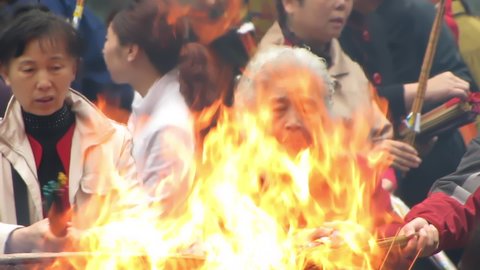HANGZHOU, CHINA, CIRCA APRIL 2009, Lingyin Temple, two women lighting joss ticks at large fire with yellow flames and heat shimmer intermittently covering their faces