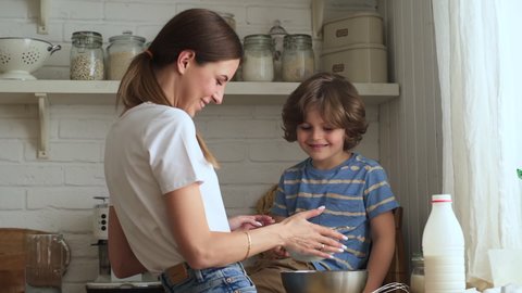 Family cooking in kitchen. Mother and son make pie cute boy looks at lady sieving flour