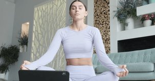 Young woman meditating, using tablet mobile app for breathing and meditation, practicing yoga watching live video learning classes on tablet. Female enjoying calm relax harmony Zen mindfulness at home