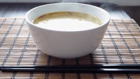 Asian hot soup in ceramic plate. Asian sticks and soup with steam on the table, side view. Video 4k resolution