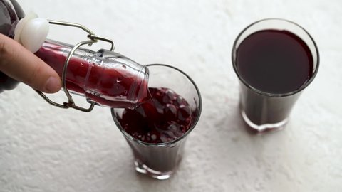 Pouring homemade black elder syrup from a bottle into a glass