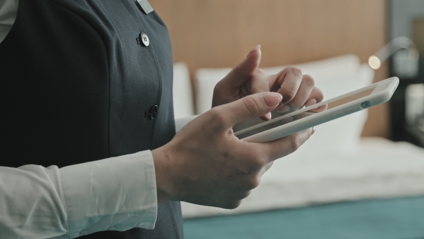 Midsection close-up of unrecognizable female hands of hotel manager using digital tablet standing inside of modern hotel room Royalty-Free Stock Footage #1077146534