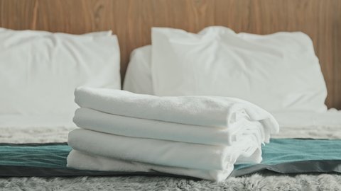 Midsection slowmo shot of unrecognizable housekeeper in uniform placing fresh white towels on bed in modern high-class hotel room preparing for guests arrival