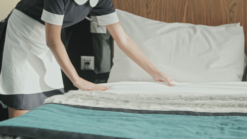 Midsection shot of unrecognizable female housekeeper in black and white uniform making bed while preparing luxury hotel room for guests | Shutterstock HD Video #1077149825