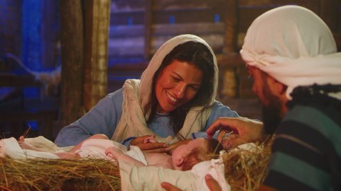 Mother Mary smiling and kissing Jesus Christ while Joseph stroking baby gently in dim inn barn in Bethlehem nativity scene