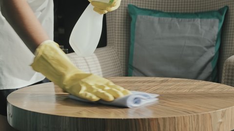 Slowmo close-up of housekeeper hands in rubber gloves cleaning and polishing surface of wooden coffee table in luxury hotel room