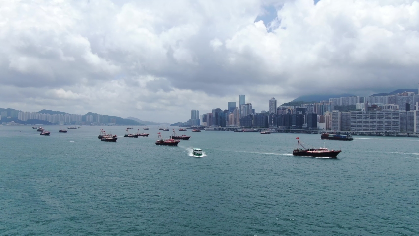 Convoy of local Fishing boats causing in Hong Kong Victoria bay, with city skyline in the horizon, Aerial view.