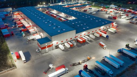 Aerial hyper lapse (hyperlapse - motion time lapse) of a logistics park with a loading hub. Semi-trailer trucks standing at warehouse ramps for loading and unloading goods at night