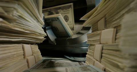 Close up shot of packs of US dollar bills lying around with cash counting machine working on background. Cash flow, business and financing 4k footage