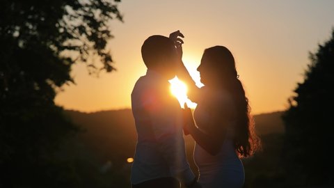 Silhouette of a young couple dancing at sunset. The sun's rays illuminate the boy and the girl. The bride revolves around herself in a dance.